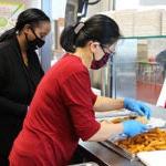 Two cafeteria supervisors prepare meals for students in a school lunch room.